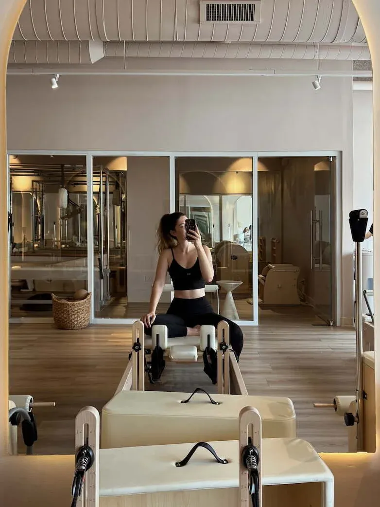 Mujer sentada en un reformer frente a un espejo